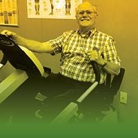 An elderly man smiles while using an exercise machine