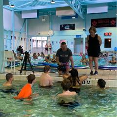 Image of youth in the leisure pool being filmed by a TV reporter with fitness instructor looking on.